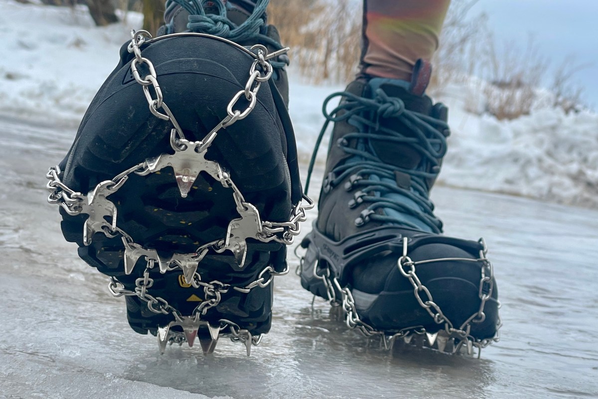 Close-up of winter boots fitted with metal traction spikes on an icy trail.