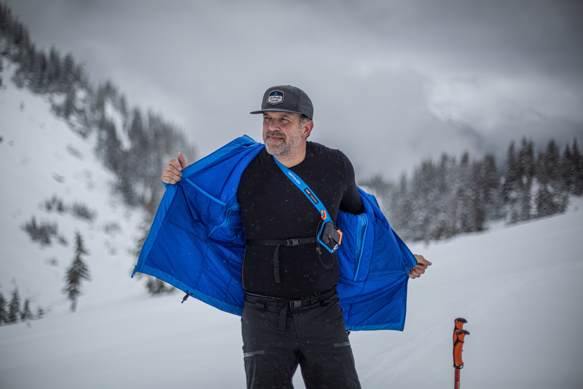 A man wearing a merino baselayer under a ski jacket on a snowy day.