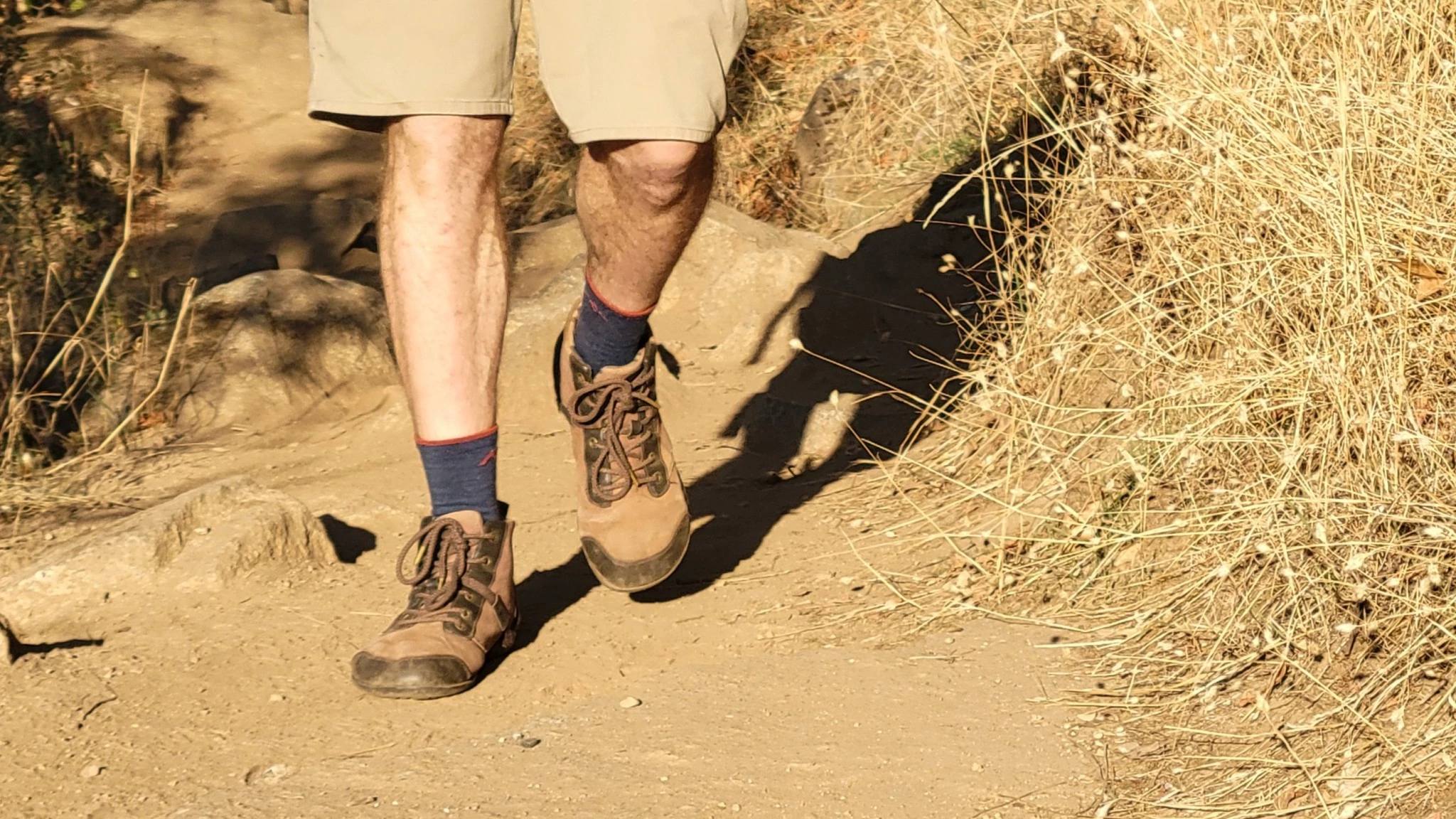 Close-up of a hiker's feet in light grey hiking socks and boots on a rocky trail.
