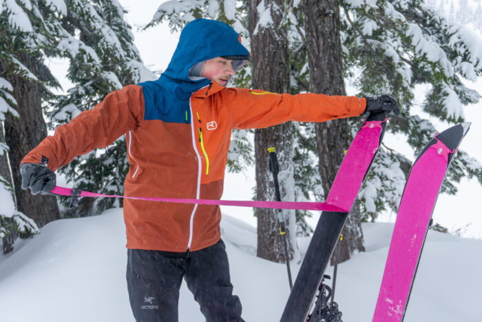 A person skinning up a mountain slope wearing a technical orange jacket.