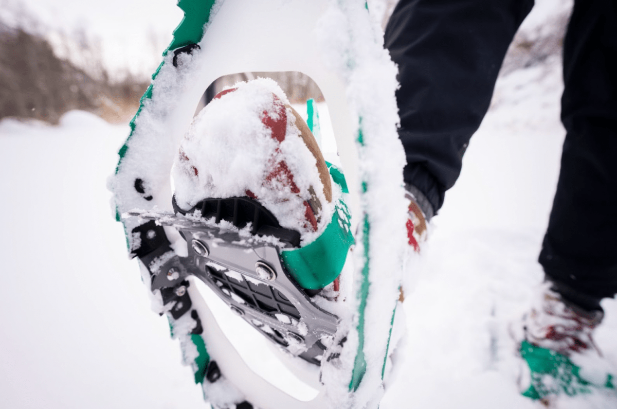 Side view of a snowshoer's boot with a metal heel riser engaged on a steep ascent.