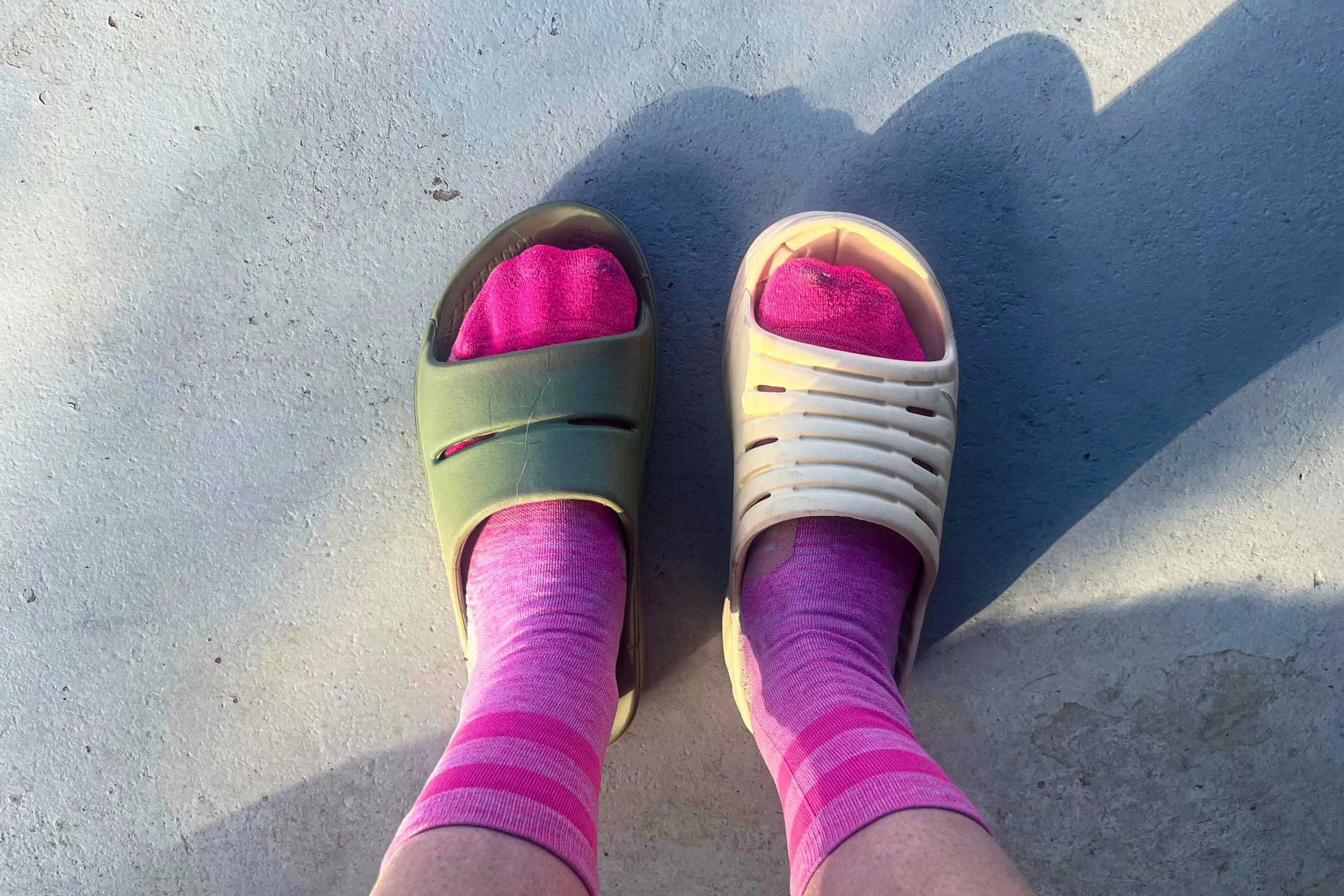 A side-by-side comparison of a thick Oofos Ooahh sandal and a bulkier Hoka Ora recovery slide.