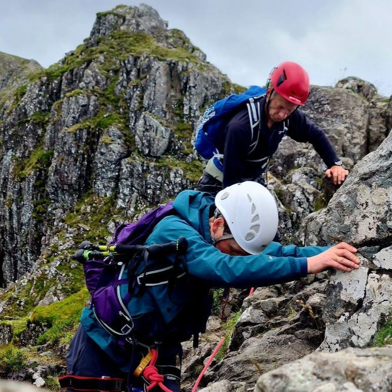 A lone climber navigating a very narrow and rocky mountain traverse.