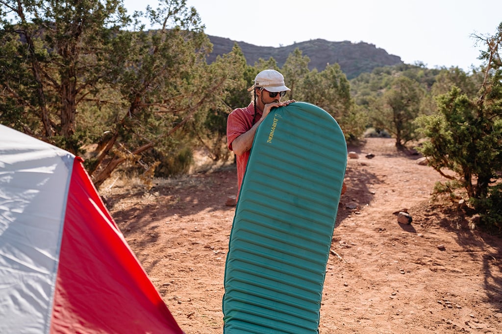 A person inflating a blue sleeping pad by mouth outdoors.