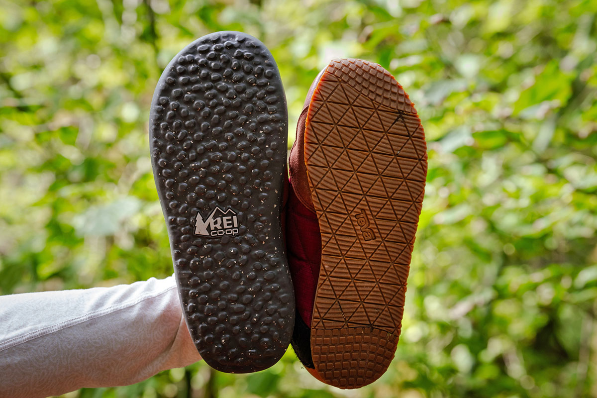 Two different camp shoe outsoles held up side-by-side to show tread patterns and lug depth.