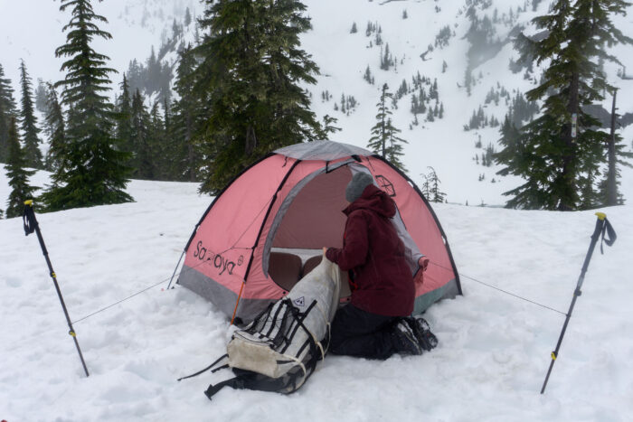 A person inflating a high-R-value sleeping pad inside a tent on the snow.