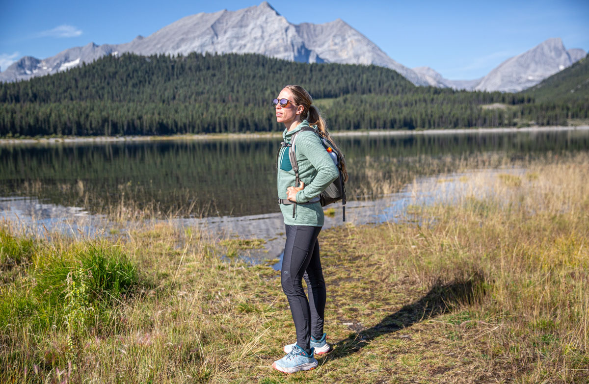 A female hiker stands near a turquoise alpine lake in the Kananaskis Wilderness wearing waterproof shoes.