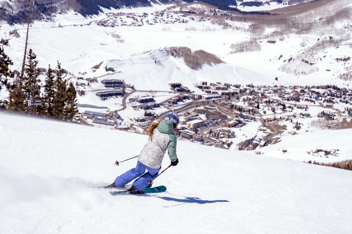 A skier adjusting the hood of her jacket over a ski helmet in windy conditions.