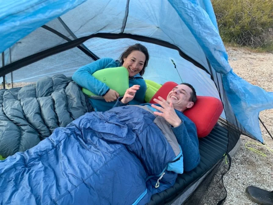 A side-by-side comparison of two hikers using different thickness backpacking pillows inside a tent.