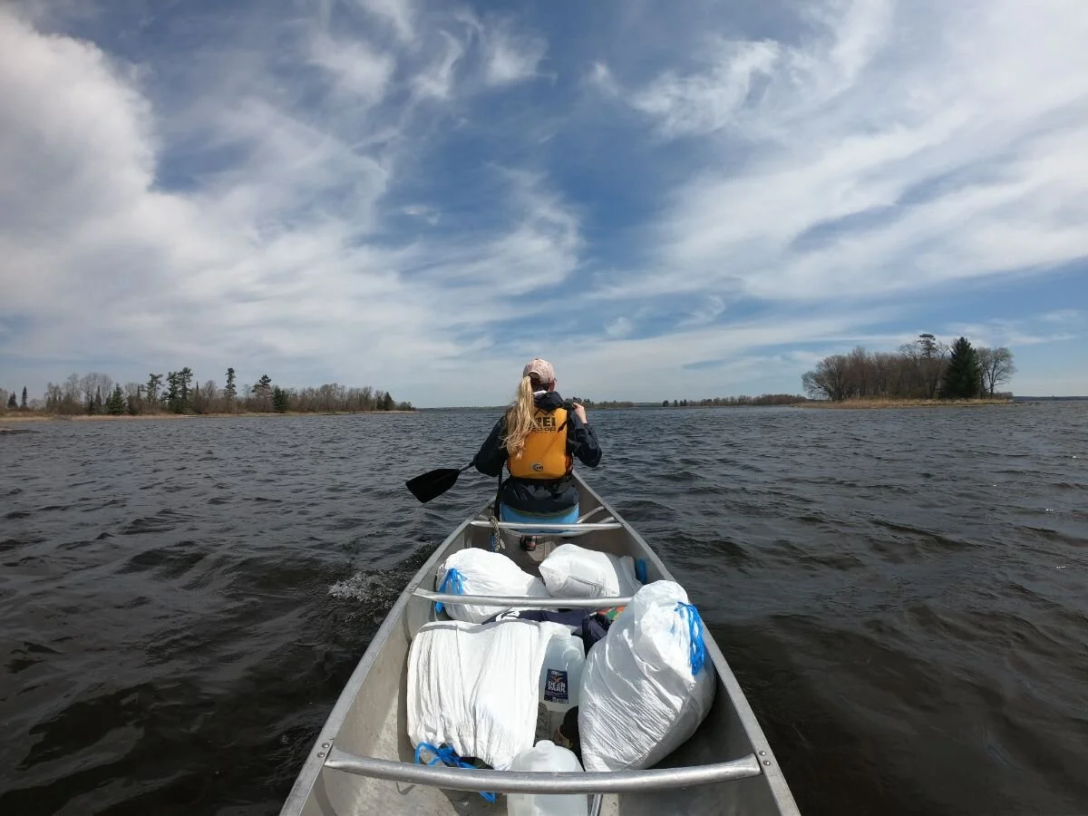 A view from a canoe looking out over the expansive blue water and distant pine-covered islands.