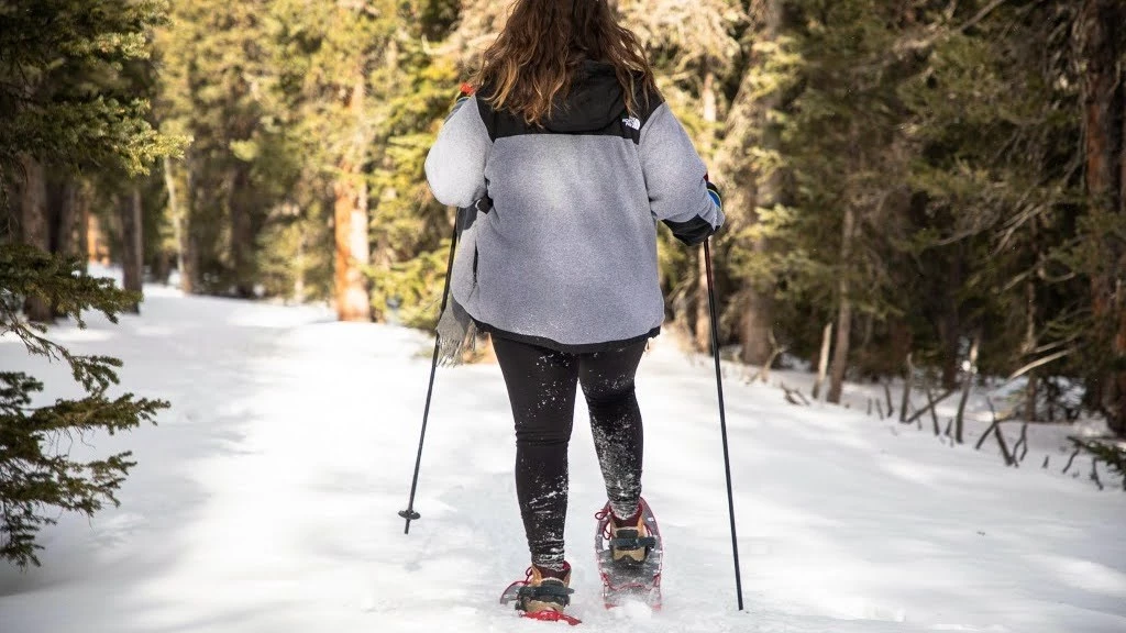 A woman using trekking poles with snow baskets for balance while hiking up a snowy slope.