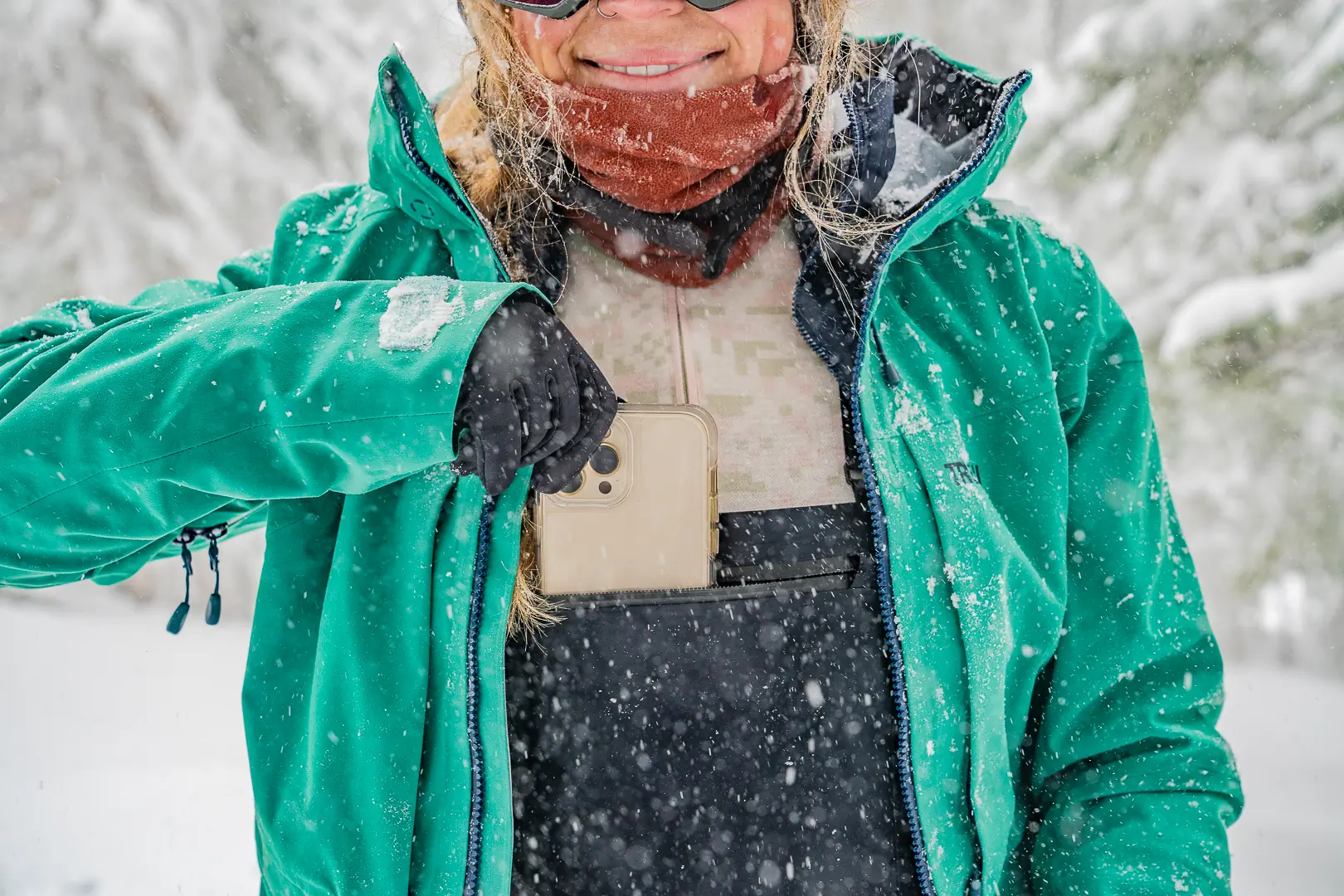 Close-up of a hand sliding a smartphone into a spacious zippered chest pocket on a pair of ski bibs.