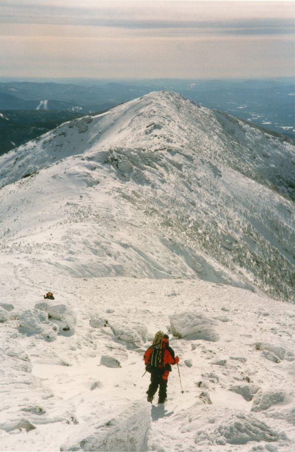 A vertical view of a snow-covered mountain peak against a bright sky.