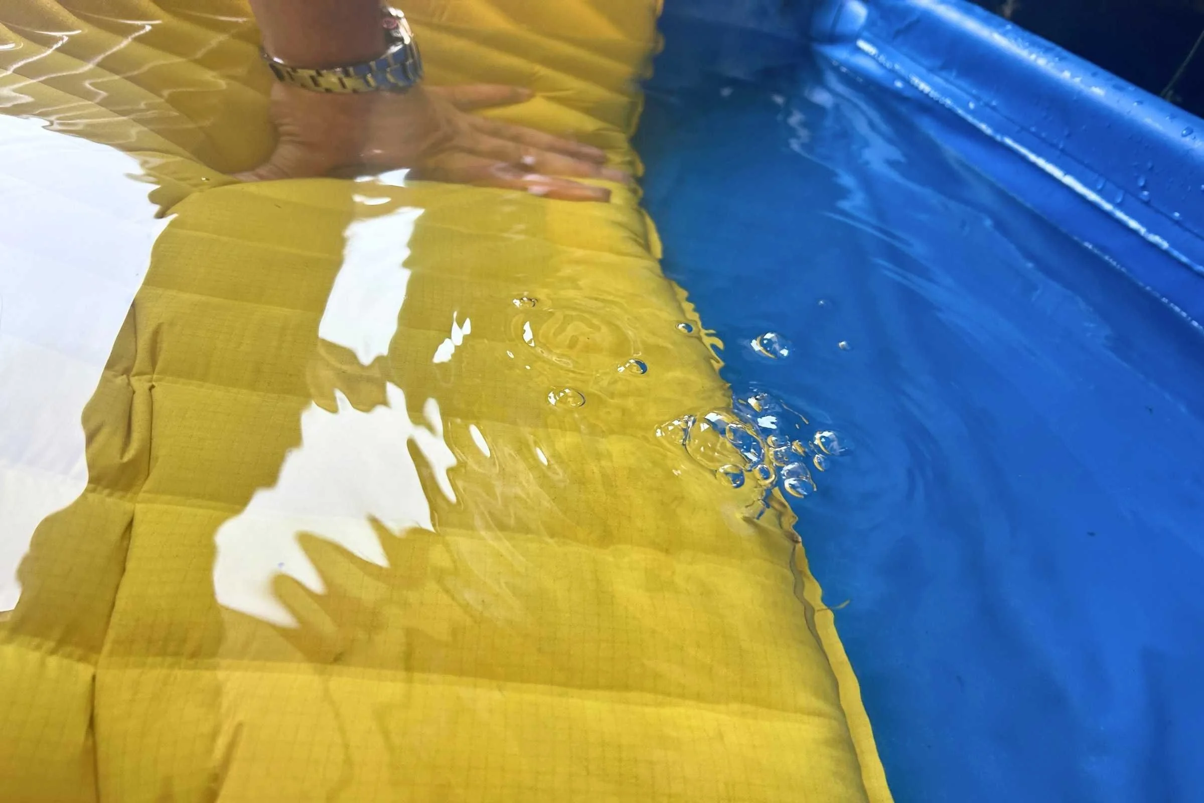 A person holding a sleeping pad underwater in a small pool to see air bubbles.