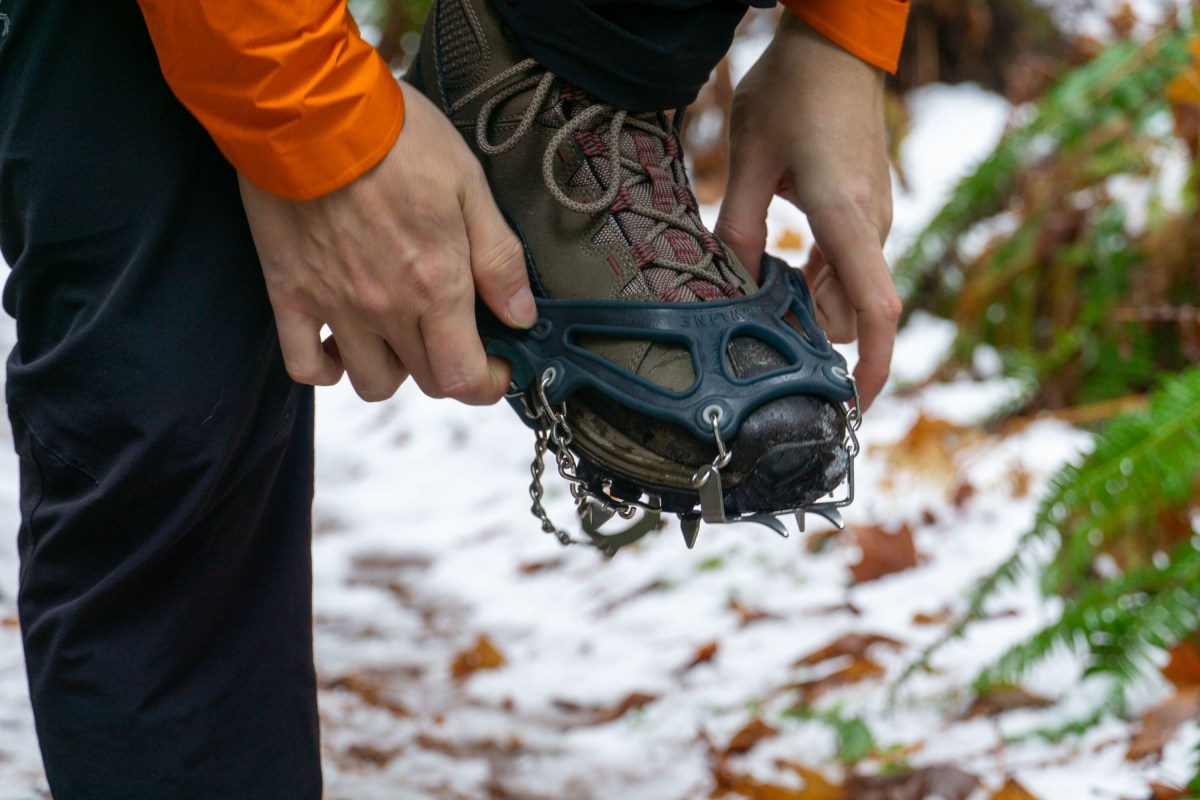 A person stretching a black rubber elastomer harness over a winter boot.