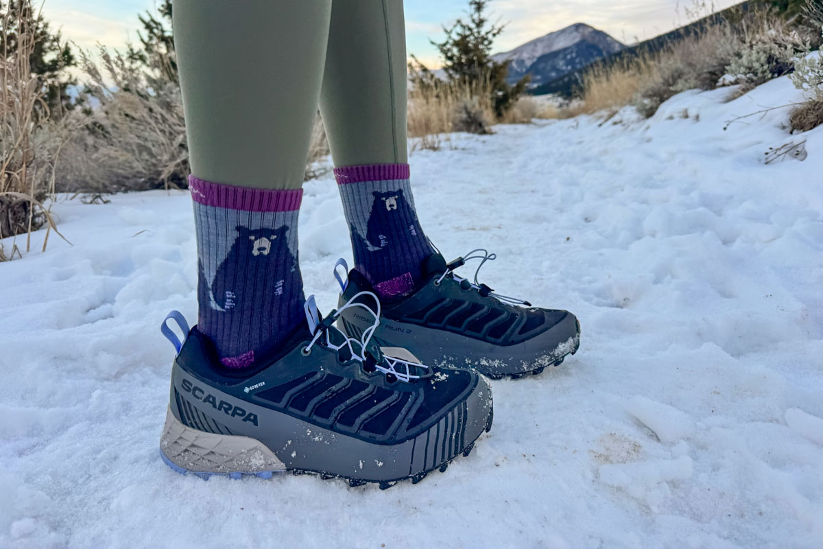 Close-up of Scarpa Ribelle Run hiking shoes standing on a snowy and rocky trail.
