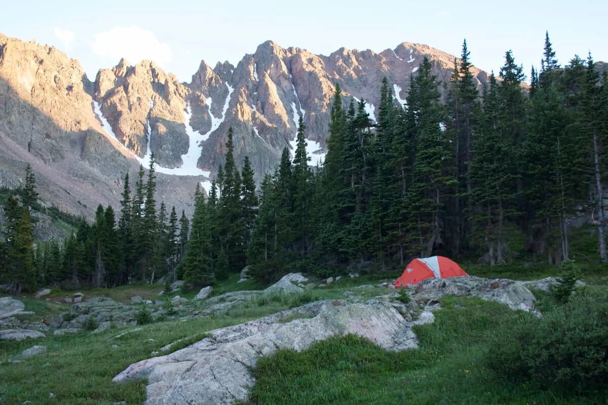 A yellow tent pitched in a scenic mountain valley during dusk.