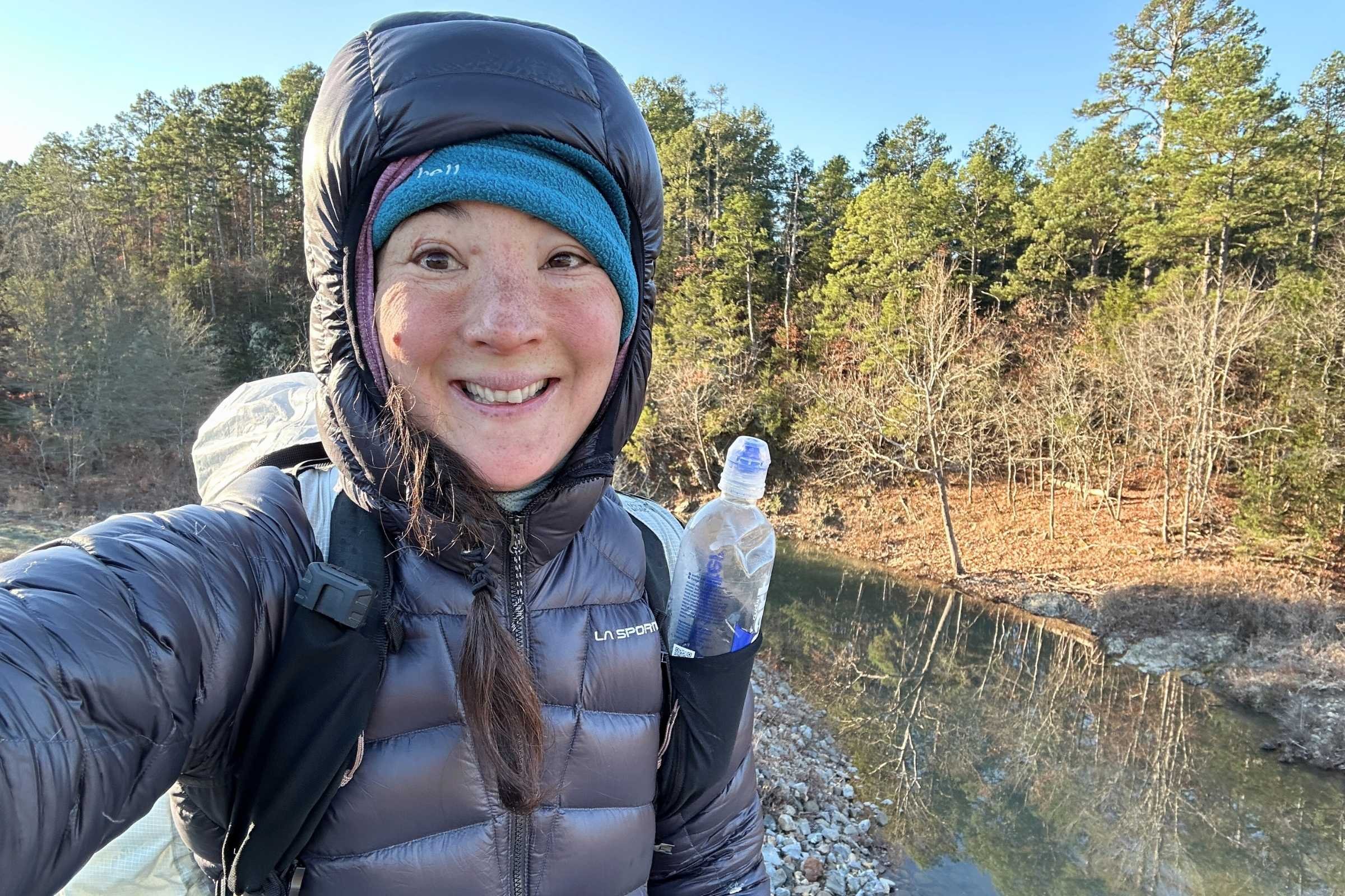 A hiker wearing a thick down jacket while trekking through a winter forest on a cold morning.