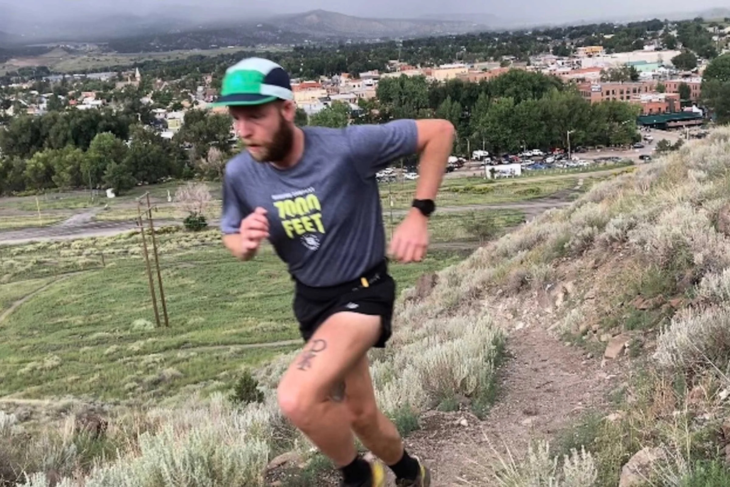 A runner wearing a blue and orange Ciele GOCap on a trail.