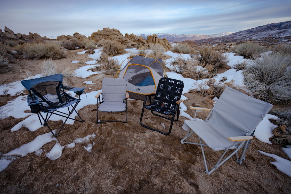 A row of various camping chairs including rockers and standard folding chairs lined up at a campsite.