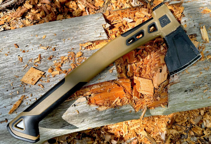 A Gerber Bushcraft Hatchet with a green handle stuck in a mossy log in the forest.
