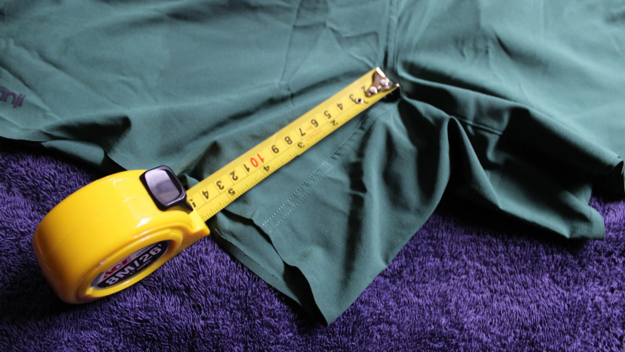 A researcher uses a tape measure to record the inseam and waistband dimensions of various running shorts on a table.