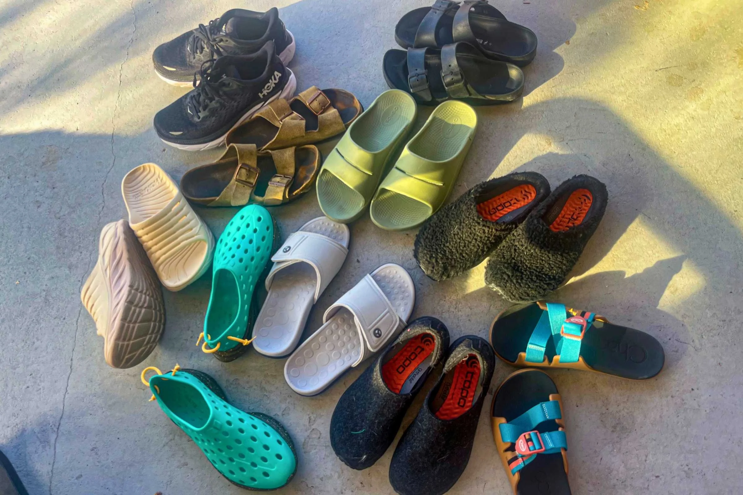 An assortment of colorful recovery slides, shoes, and sandals laid out on a wooden surface.