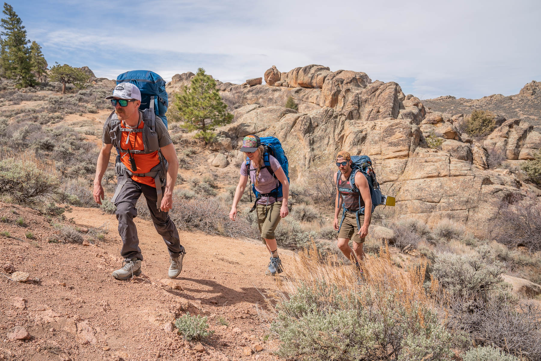 Geat testers Morgan Tilton and Adam Ruggiero evaluating various hiking boots in a grassy field near mountains.