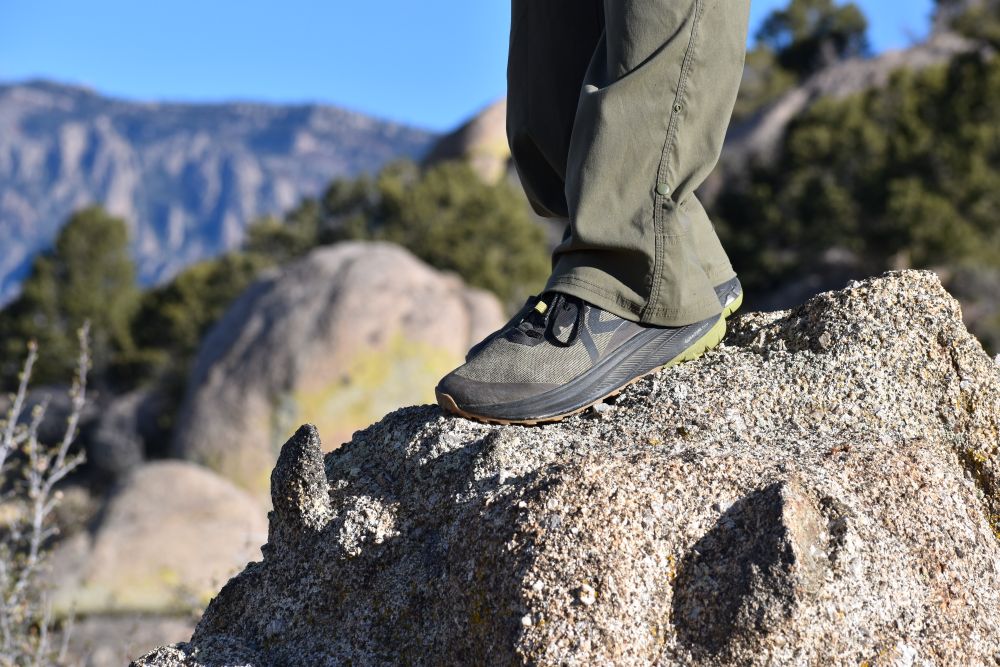 Side profile of a green KEEN Roam trail runner against a natural mountain background.