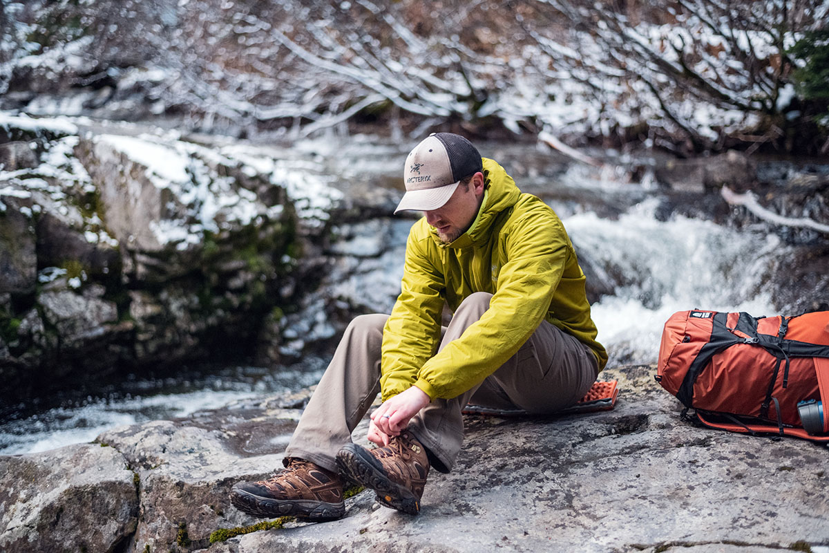A person kneeling to adjust hiking boots while wearing an Arc'teryx Atom hoody.