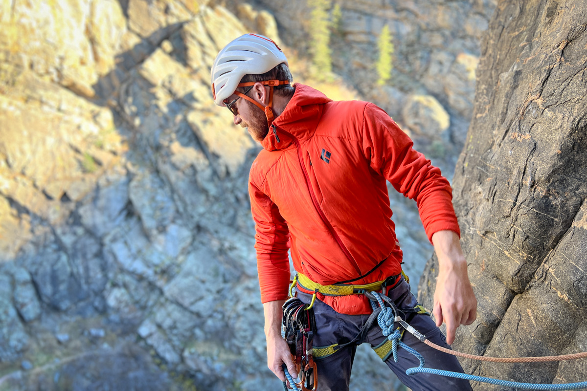 A man rock climbing on a steep granite face while wearing a flexible synthetic insulated jacket.