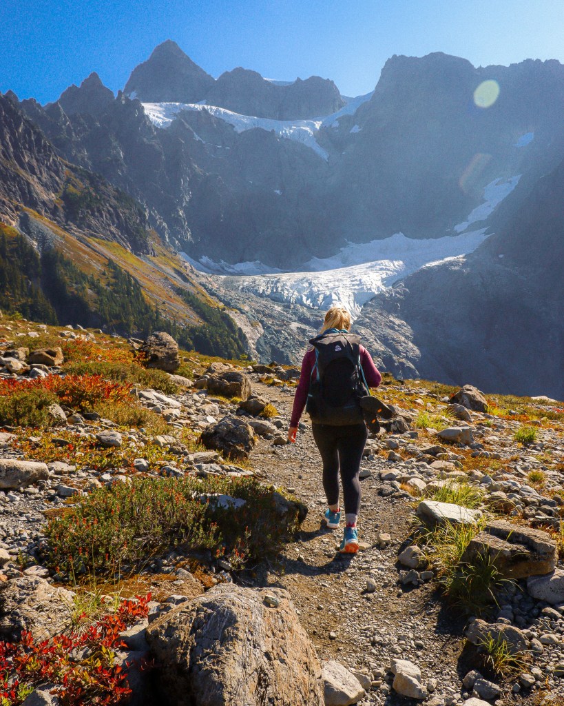 A hiker wearing KEEN Zionic hiking shoes walking toward a scenic mountain glacier.