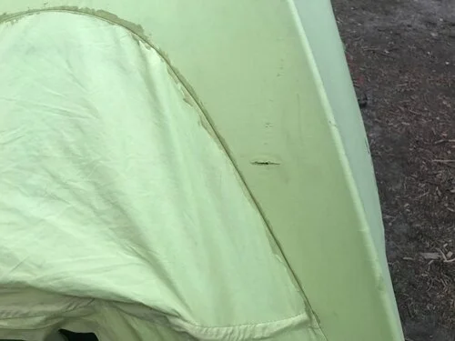 Close-up of a jagged L-shaped tear in green nylon tent fabric.
