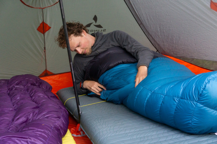 A tester adjusting the tension straps on a technical sleeping quilt to minimize dead air space.