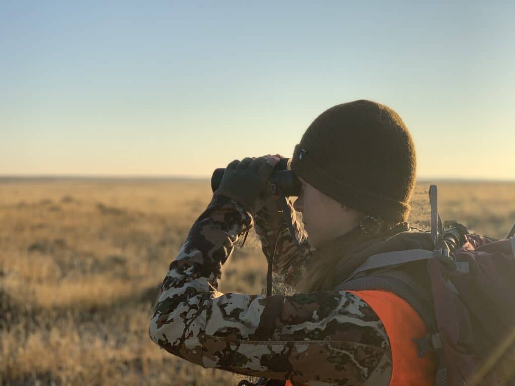 Hunter with rifle overlooking a vast open plains landscape.
