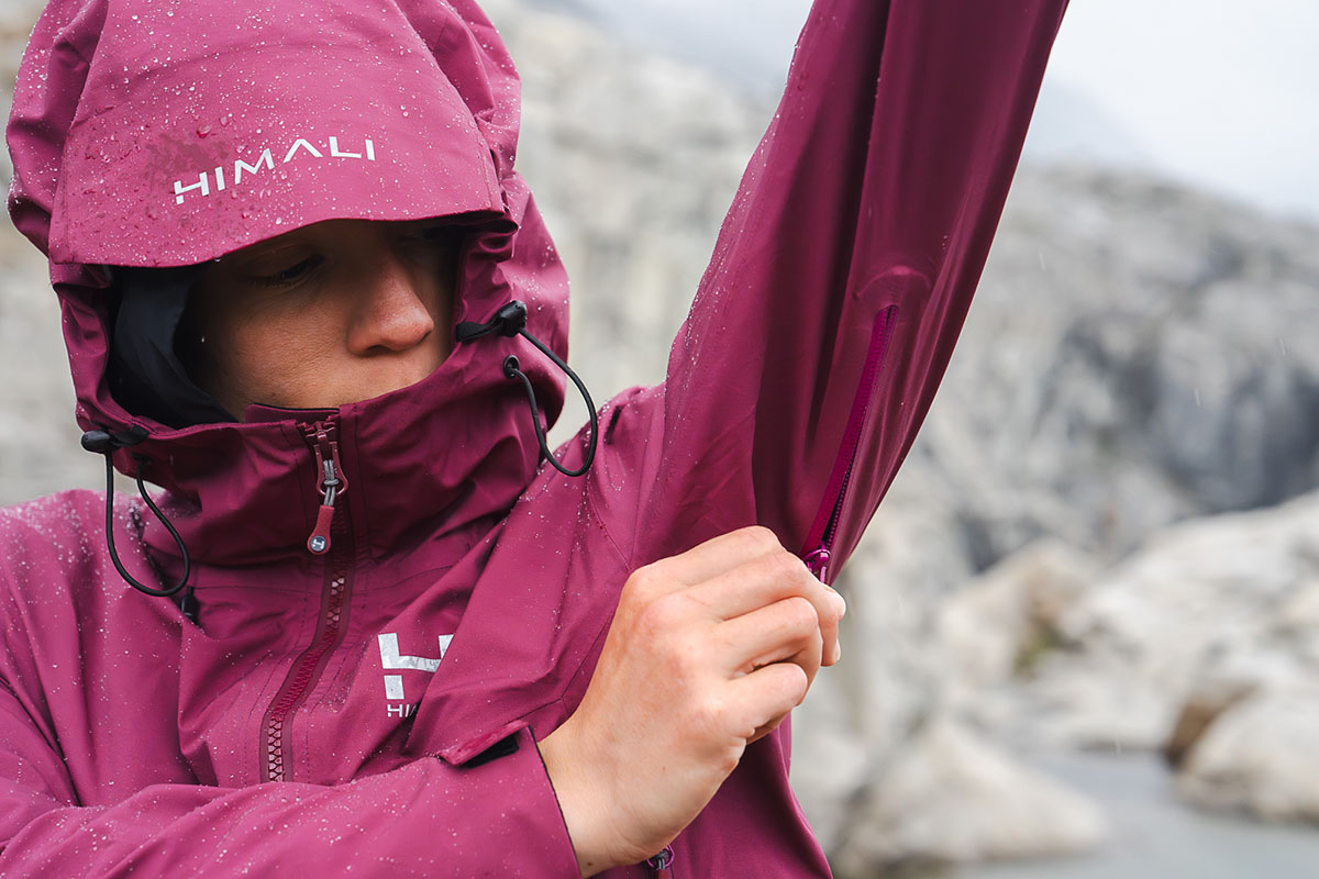 A close-up of a woman unzipping the underarm pit zip of a yellow hardshell jacket.