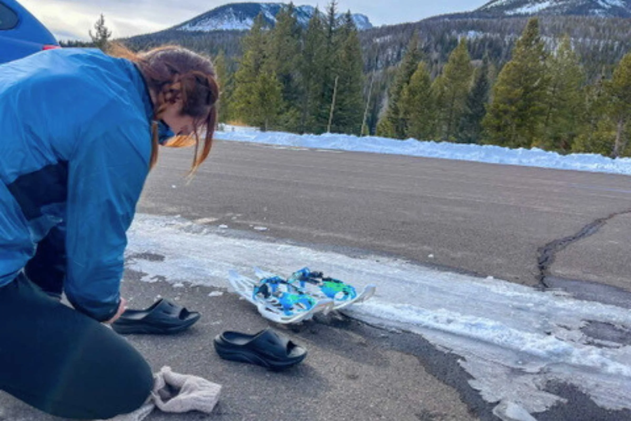 A person lacing up Hoka Ora recovery slides while sitting in the snow in Rocky Mountain National Park.