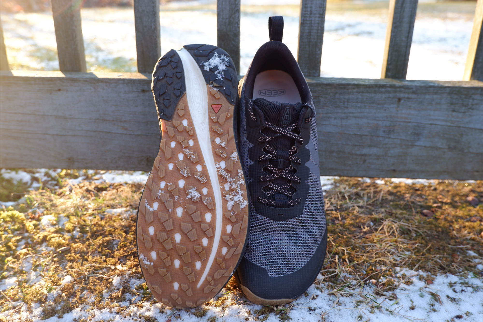 One KEEN Roam shoe flipped upside down showing its outsole next to its pair on a snowy surface.