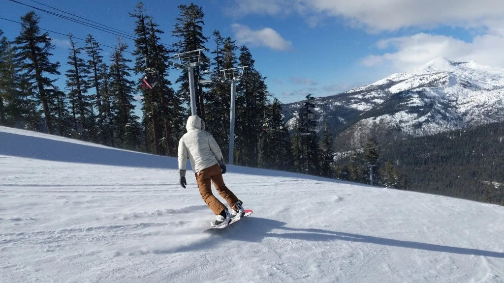 Two people in base layers standing on a snowy hillside with skis.