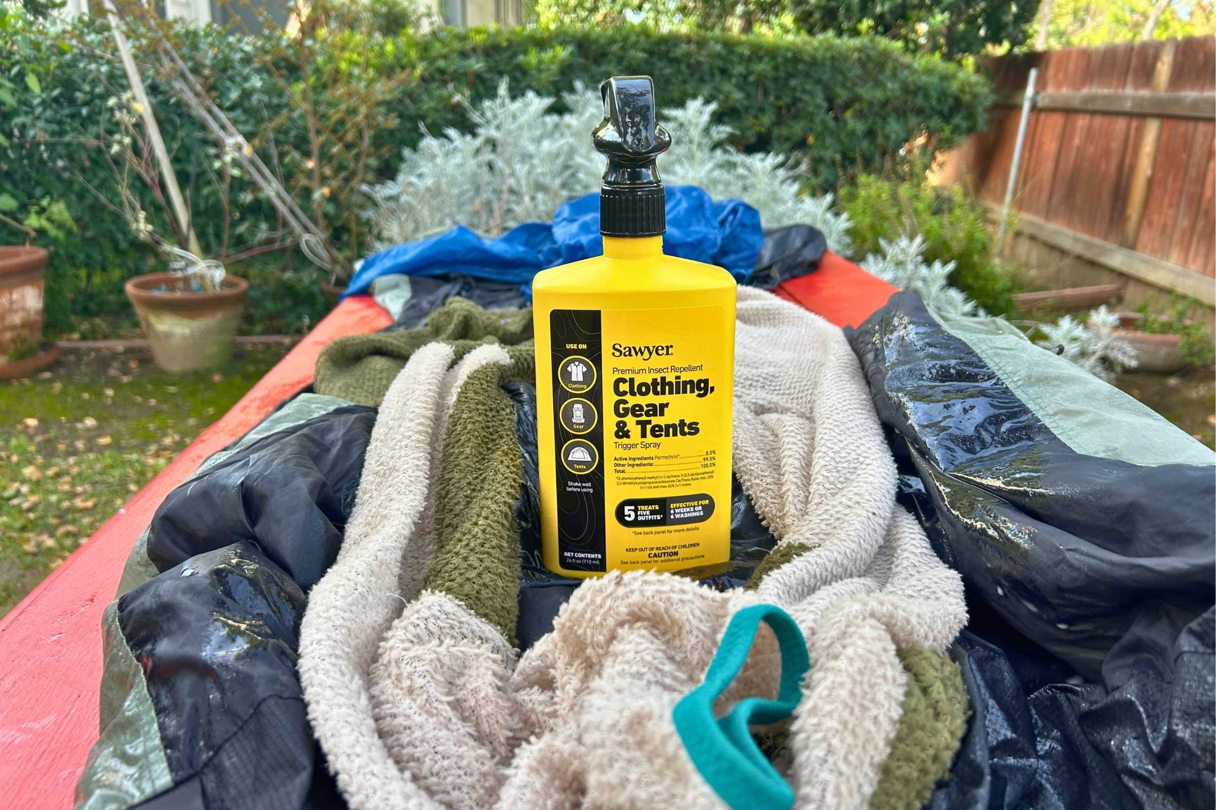 A hiker preparing gear by treating various clothing items with Permethrin.
