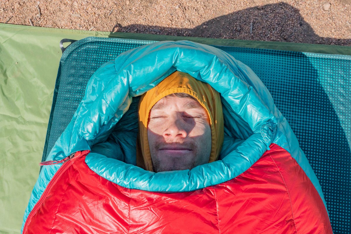 A climber deeply tucked into the mummy hood of a high-loft down sleeping bag.