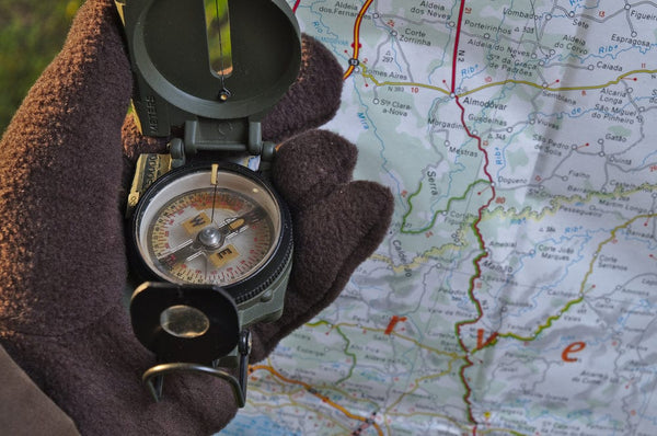 A topographical map and a traditional baseplate compass resting on a snowy surface.