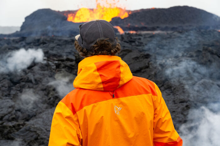A person in a Norrona hardshell jacket standing near an active volcano area in Iceland.