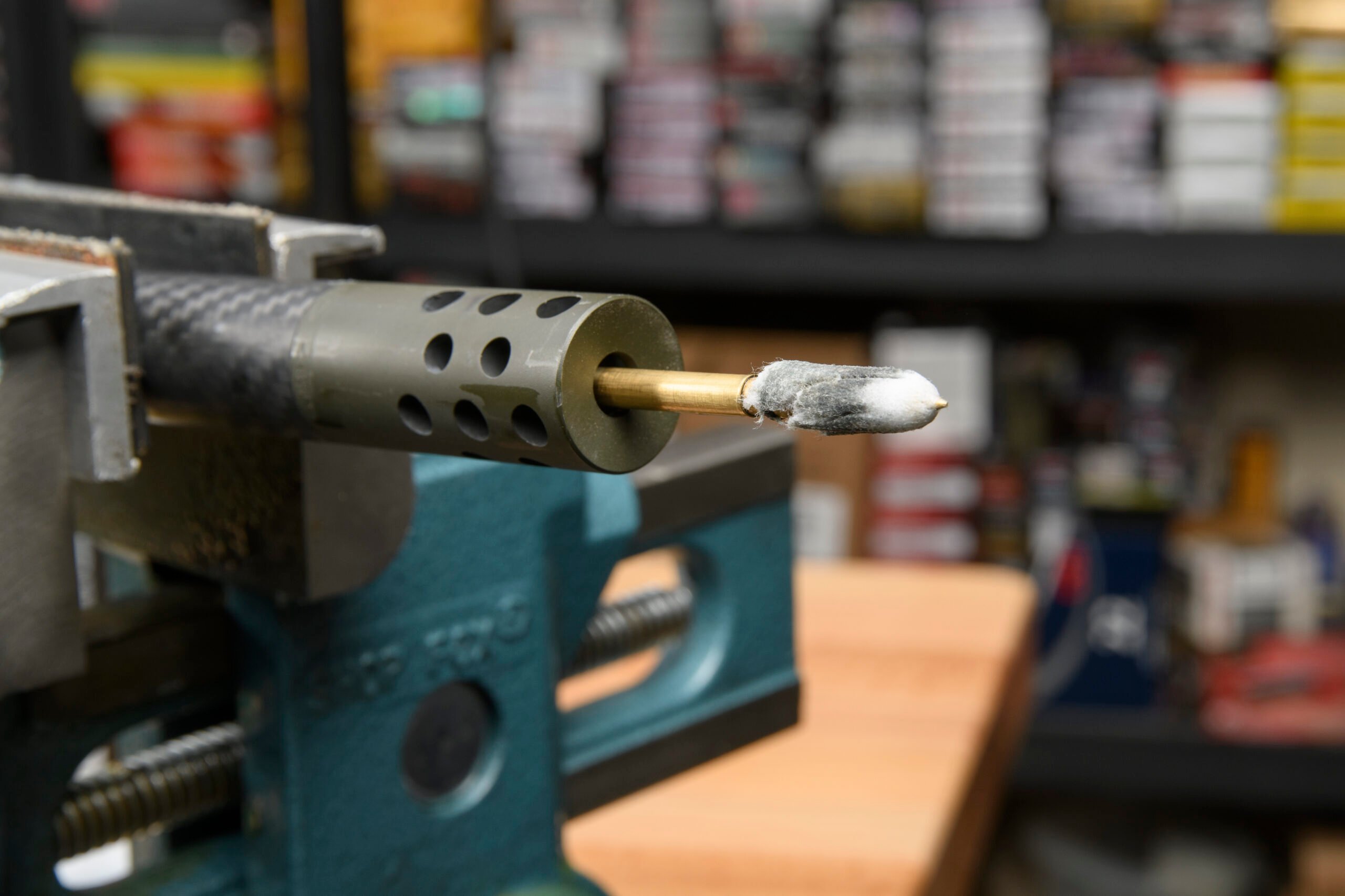 A white cleaning patch exiting the muzzle of a rifle barrel wrapped in carbon fiber.