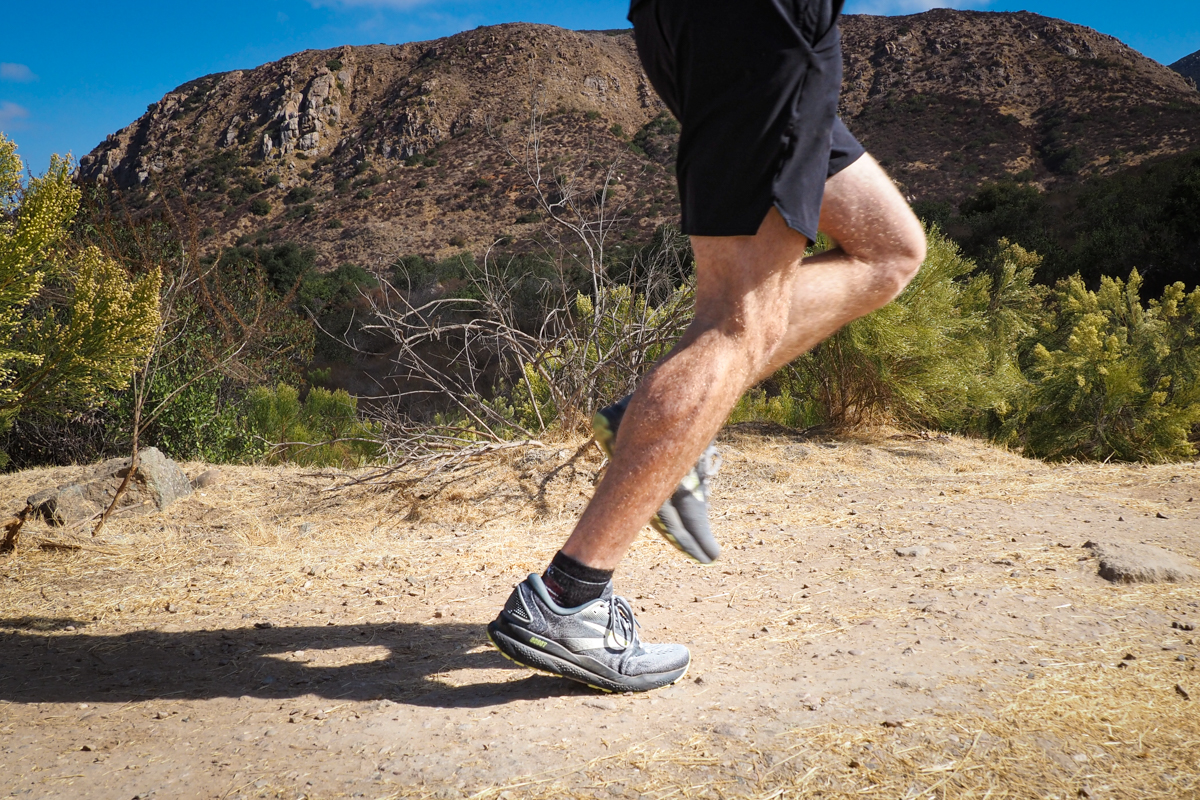 A male runner wearing Brooks Ghost 17 shoes on a well-maintained dirt path.