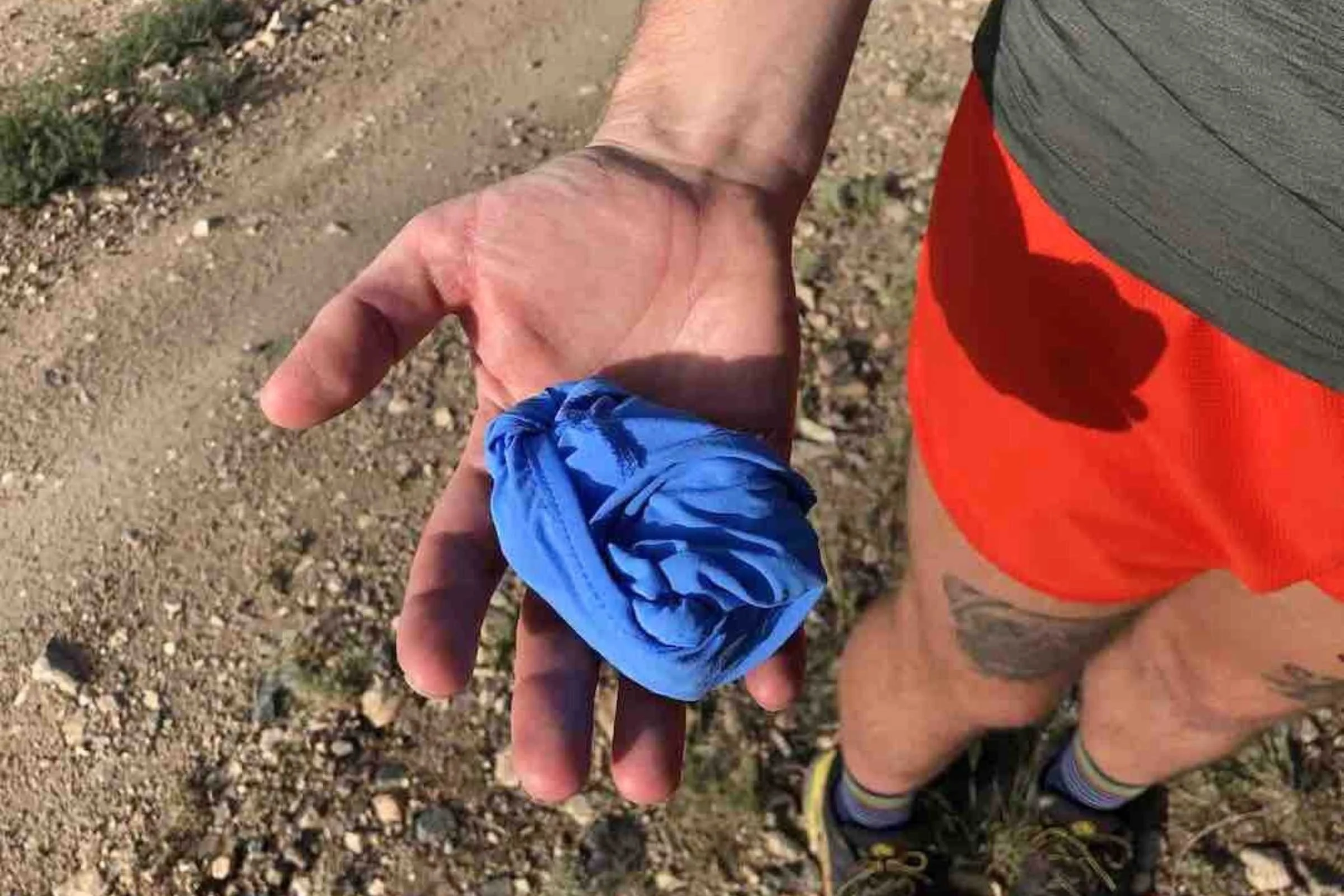 A hand holding the Brooks Lightweight Packable hat folded into its own rear pocket.