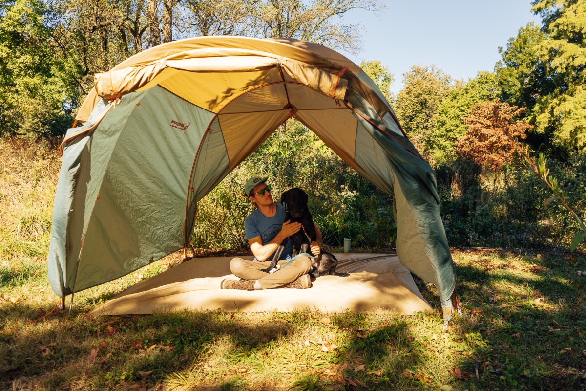 A person and a dog relaxing under the large extended vestibule awning of the tent
