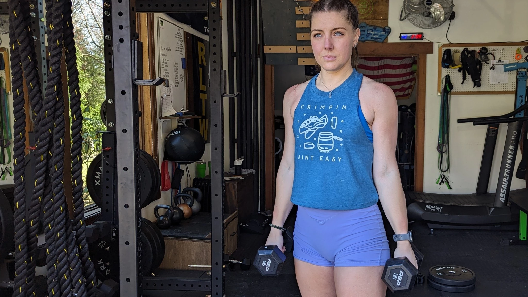 A person lifting a rubber-coated dumbbell in a garage gym environment.