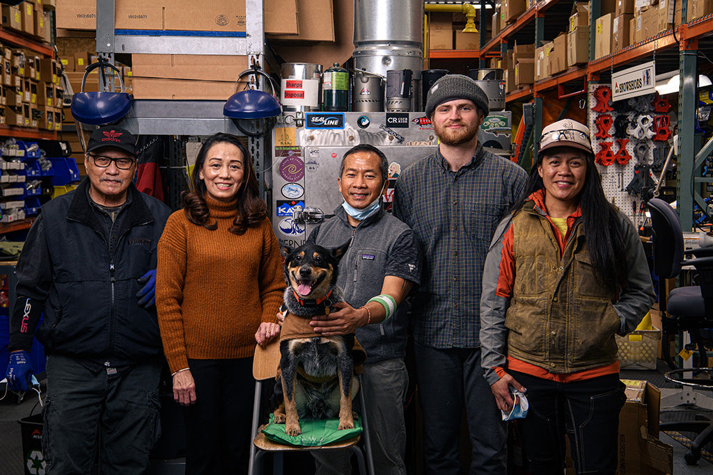 Two technicians working on outdoor gear in a professional repair warehouse.