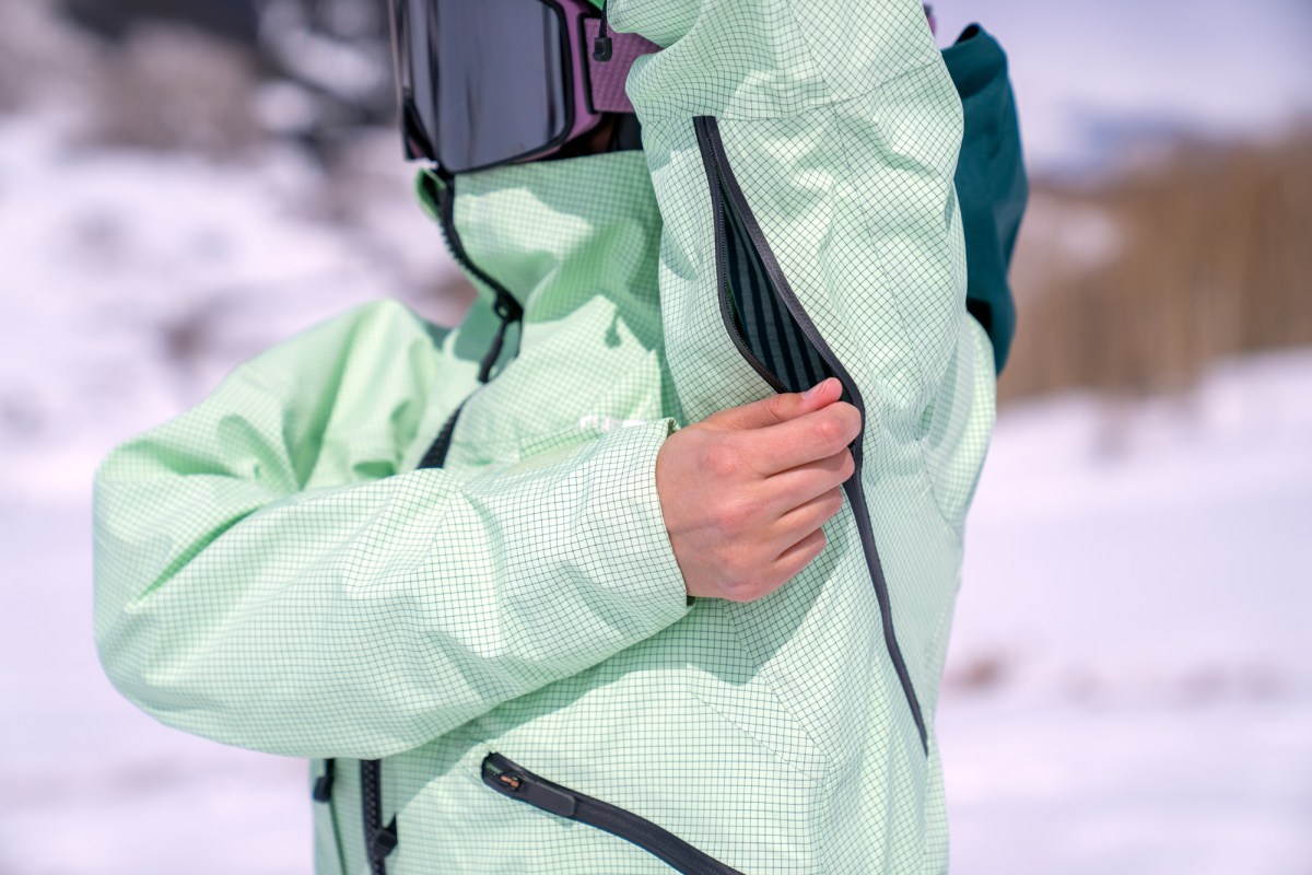 Close-up of a skier opening the underarm ventilation zipper of a ski jacket.